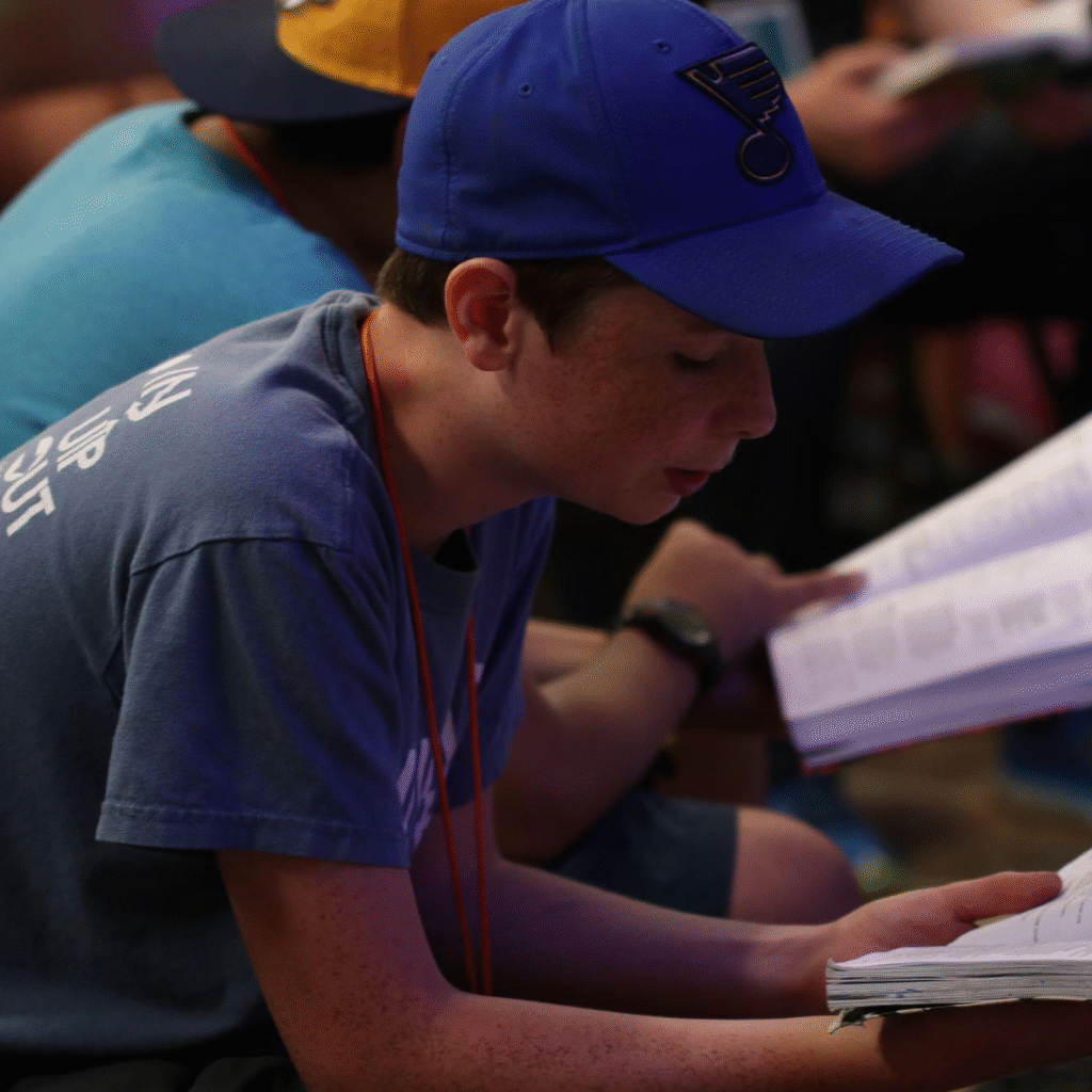 Teen leading a devotional during a summer ministry event, supported by an adult mentor.