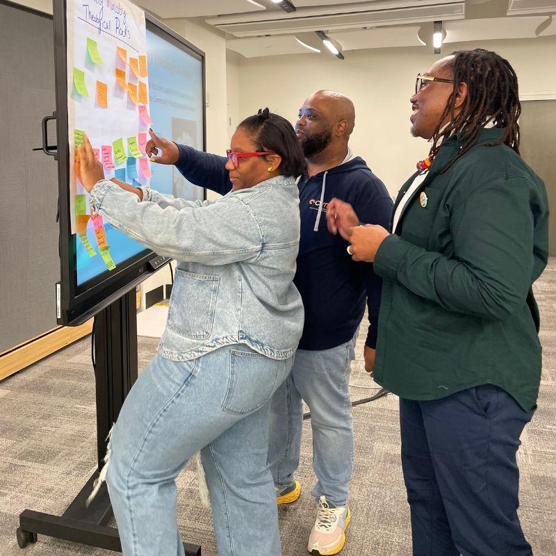 Three African-American adults are using a whiteboard and sticky notes to brainstorm new ideas.