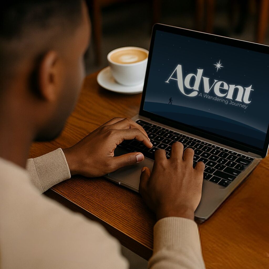 Side profile of a black man typing on a laptop with an advent graphic in the screen. There's a white coffee cup and saucer to the left of the computer.