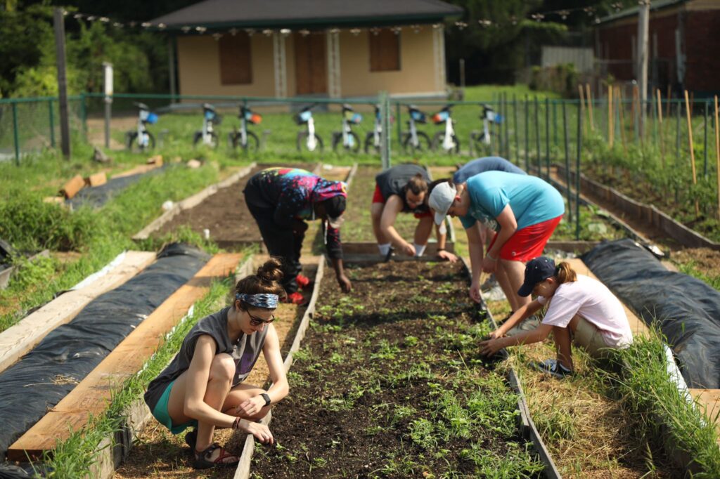 group of people kneeling around a raised garden bed and digging in the dirt. One of the benefits of youth mission trips is learning how to work together to accomplish a common goal.